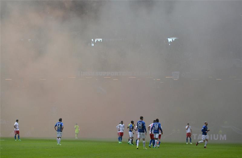 Die Spieler beider Mannschaften stehen während einer Spielunterbrechung wegen Pyrotechnik auf dem Feld. Foto: Daniel Reinhardt/dpa