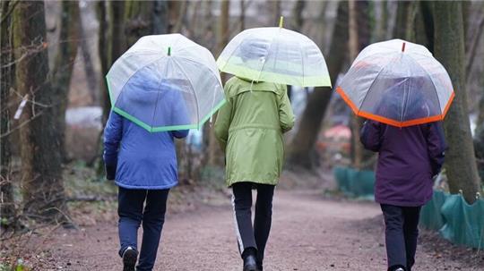 Drei Frauen gehen mit Regenschirmen spazieren.