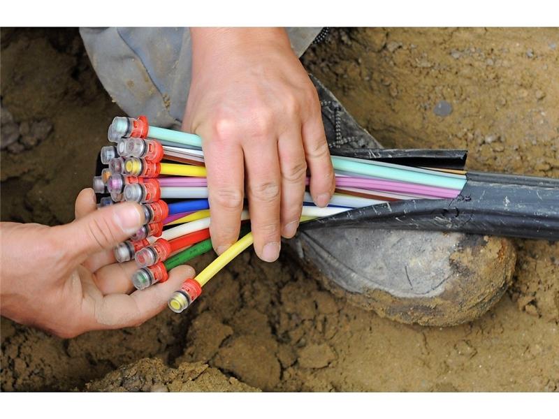 Ein Bauarbeiter fächert ein Glasfaser-Kabel mit farbigen Einzelsträngen auseinander. Wer damit versorgt ist, hat mit Internet-Verbindungen keine Probleme. Doch nicht alle Haushalte kommen in diesen Genuss. Kneffel/dpa