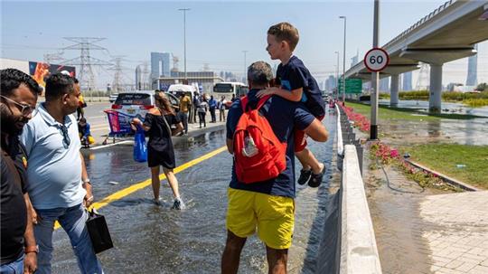 Ein Mann trägt ein Kind durch das von starkem Regen verursachte Hochwasser in Dubai.