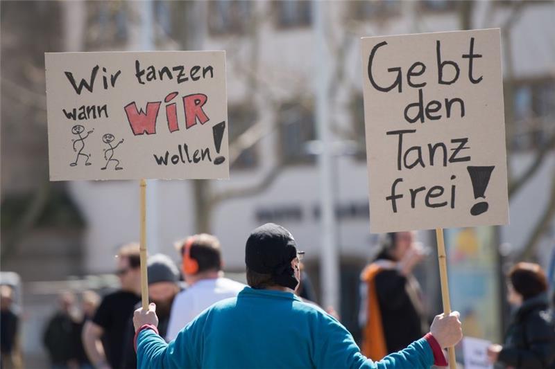 Ein Teilnehmer einer Versammlung gegen das Tanzverbot hält am 3. April in Stuttgart (Baden-Württemberg) Schilder mit der Aufschrift "Wir tanzen wann wir wollen!" und "Gebt den Tanz frei". Foto Wolfram Kastl/dpa