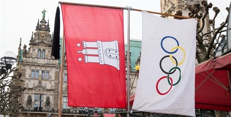 Ein Trauerflor an einer Flagge mit dem Wappen von Hamburg und eine Flagge mit den Olympischen Ringen hängen am Rathausmarkt in Hamburg. Foto Charisius/dpa