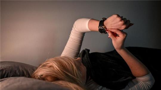 Eine Frau stellt im Bett ihre Armbanduhr um.