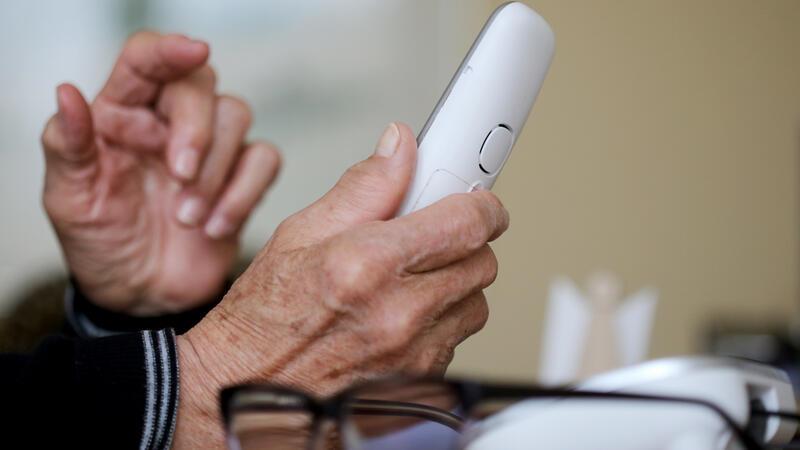 Eine ältere Frau hält ein Telefon in der Hand.