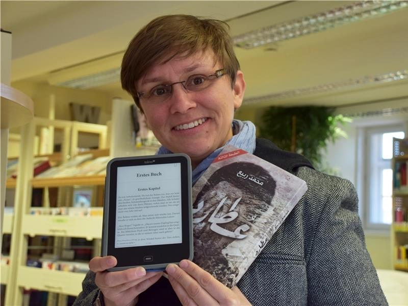 Janina Kolb zeigt ein Lesegerät, auf dem die erste Seite aufgeschlagen ist und eines der neuen Bücher aus der Fremdsprachenabteilung.