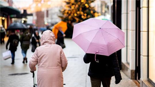 Menschen gehen bei regnerischem Wetter mit Regenschirmen durch die Innenstadt.