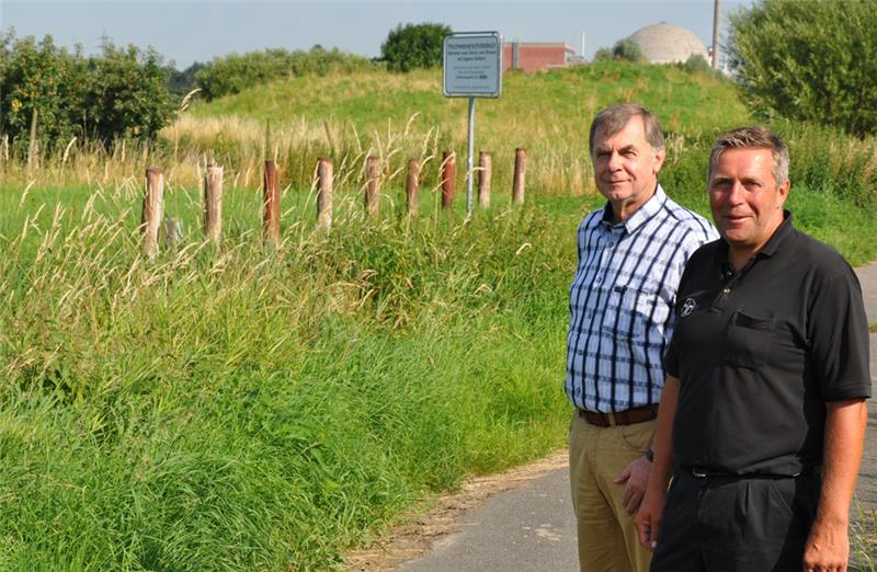 Wo jetzt der Hügel hinter Bauamtsleiter Rolf Riggers (links) und Bürgermeister Timo Gerke zu sehen ist, soll der neue Parkplatz entstehen, auf dem Grünstreifen vorne im Bild neben dem Radweg die Zufahrt. Foto: Lankuttis