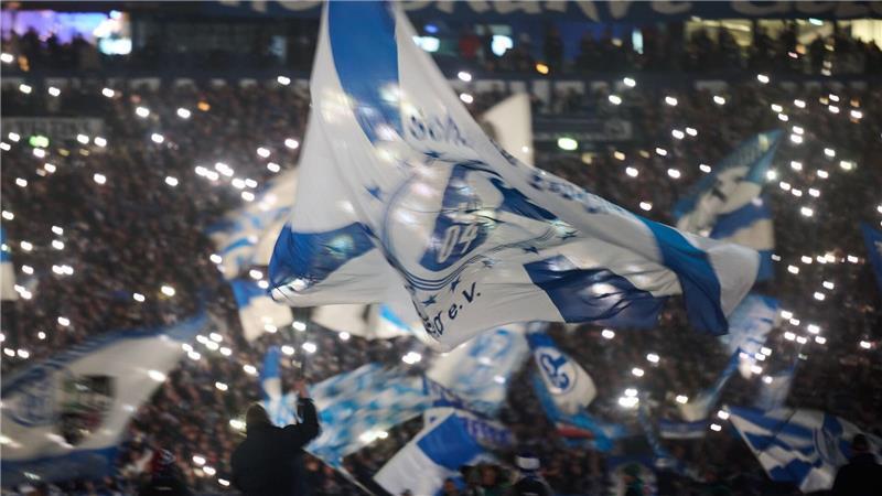  Eine Schalker Vereinsfahne weht vor dem Spiel gegen den 1. FC Magdeburg vor den Lichtern von Smartphones.