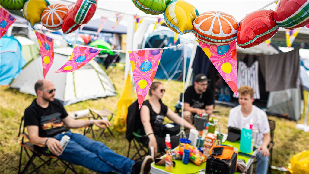 21.06.2024, Niedersachsen, Scheeßel: Festivalbesucher sitzen auf dem Zeltplatz d...