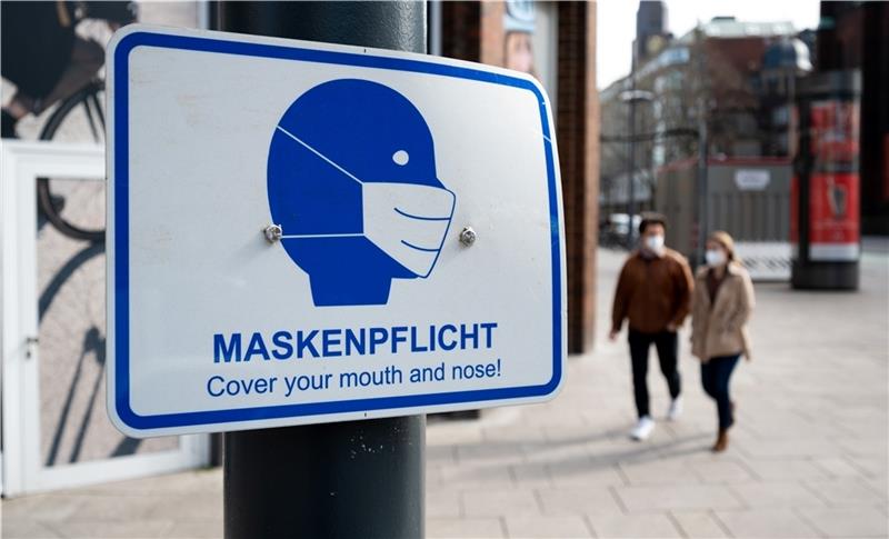 29.03.2021, Hamburg: Passanten gehen in der Innenstadt an einem Schild mit der Aufschrift „“Maskenpflicht““ vorbei. Seit Mitternacht gilt in Hamburg eine neue Corona-Verordnung. Mit der Verfügung verlängert der Senat den Lockdown bis zum 18