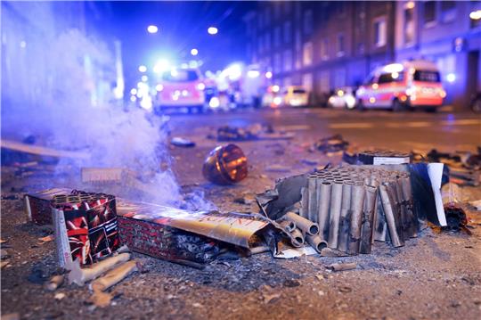 Abgebrannte Böller liegen nach der Silvesternacht auf einer Straße, während im Hintergrund Einsatzkräfte der Feuerwehr stehen. Foto: David Young/dpa