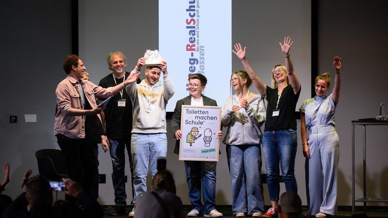 Schulen für saubere Toiletten ausgezeichnet Abgesandte der Hellweg Realschule in Unna-Massen (Nordrhein-Westfalen) stehen zusammen mit Moderator „Checker“ Julian Janssen (l) bei der Verleihung der Hauptpreise des bundesweiten Wettbewerbs „Toiletten machen Schule“ beim 1. Deutschen Schultoilettengipfel der German Toilet Organization (GTO) auf der Bühne.