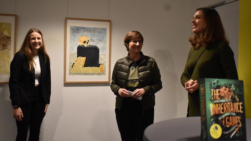 Buxtehuder Bulle: Verleihung ohne Gewinnerin Jennifer Lynn Barnes Abiturientin Amelie Gabriel und Lehrerin Franziska Sopha erklären Bürgermeisterin Katja Oldenburg-Schmidt (Mitte) details zu den gestalteten Buchcovern im Rahmen des Themas Illustration.
