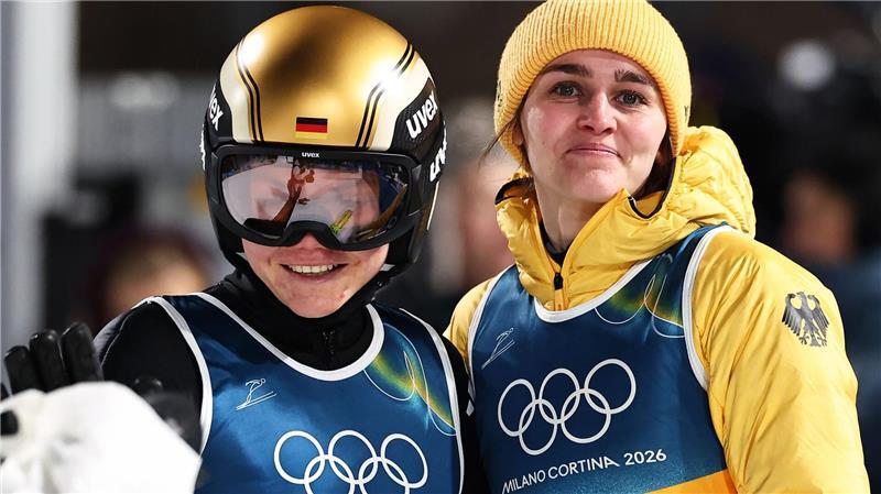 Agnes Reisch (l, Deutschland) reagiert nach ihrem Sprung von der Großschanze neben Teamkollegin Selina Freitag (Deutschland) bei den Olympischen Winterspielen Mailand Cortina 2026.
