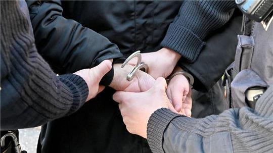 Einem Mann werden von zwei Polizisten Handschellen angelegt.