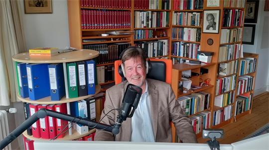 Am Computer, umgeben von Bücherregalen, arbeitet Matthias von Hellfeld jeden Tag, auch am Wochenende. Nachschlagewerke, Bücher, Kopfhörer und Mikrofon gehören zu seinem Handwerkszeug.