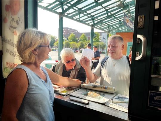 Am Fenster des Kiosks zeigt Marion Boje das Foto von sich im TAGEBLATT vom Montag. Den Stammkunden Gisela und Alex gefällt‘s. Foto: Richter