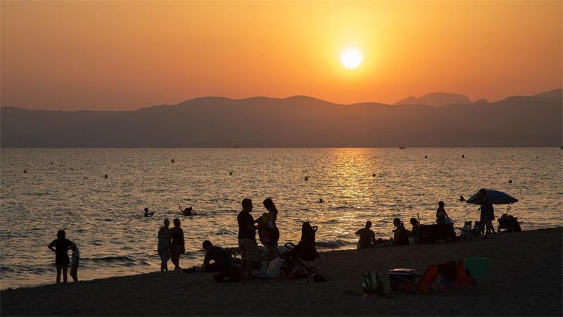 Am Strand von Playa de Palma auf Mallorca baden Menschen bei Sonnenuntergang im Meer. (Archivbild)