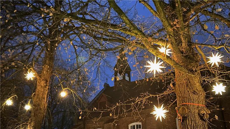 An den winterlich kahlen Baumkronen vor der Himmelpfortener Kirche leuchten Herrnhuter Sterne.