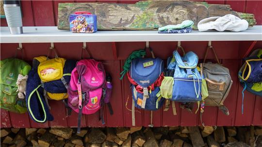 An einem Bauwagen hängen die Kinder eines Waldkindergartens ihre Rucksäcke auf.