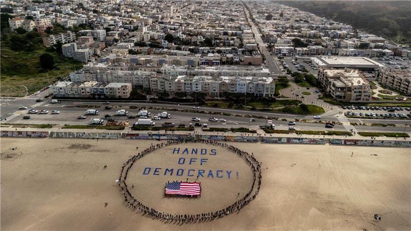 Landesweite Proteste gegen Trump in den USA An einem Strand im Bundesstaat Kalifornien bildeten Demonstranten einen menschlichen Kreis um eine US-Flagge und den Slogan „Hände weg von der Demokratie!“.