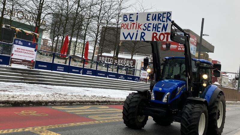 An einem Traktor ist ein Schild mit der Aufschrift "Bei eurer Politik sehen wir Rot" zu sehen.