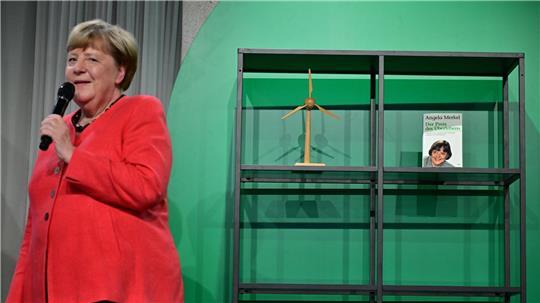 Angela Merkel (CDU), Bundeskanzlerin a.D. und ehemalige Bundesumweltministerin, spricht auf der Bühne beim Festakt „Seit 40 Jahren NaturVerbunden“ zum 40. Jubiläum des Bundesumweltministeriums im Café „Moskau“, während im Hintergrund ihr Buch mit dem Titel „Der Preis des Überlebens“ zu sehen ist.