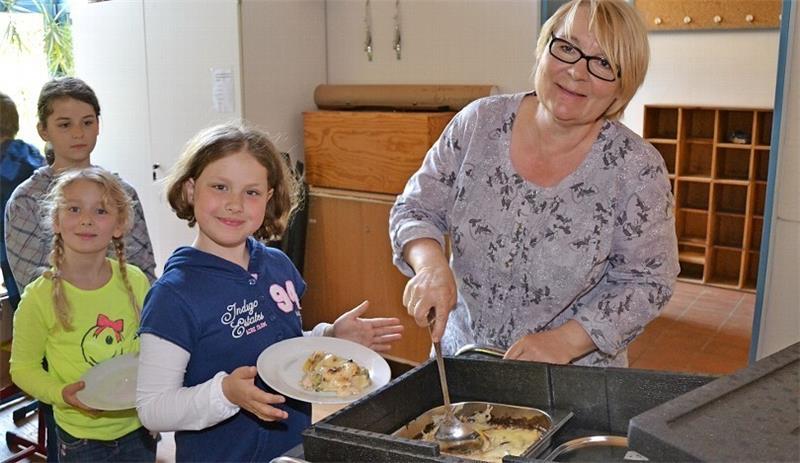Angelika Holzhausen portioniert Kartoffelauflauf auf den Tellern von Jana (Mitte) und Lina.