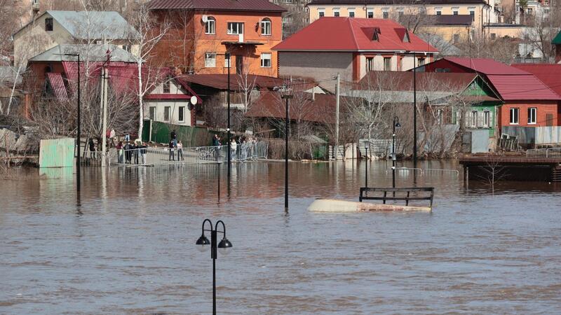 Anwohner stehen an einer Absperrung und beobachten ein überschwemmtes Gebiet im russischen Orenburg.