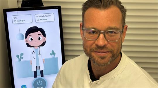 Apotheker Alexander Stüwe sitzt neben dem Telemedizin-Terminal.