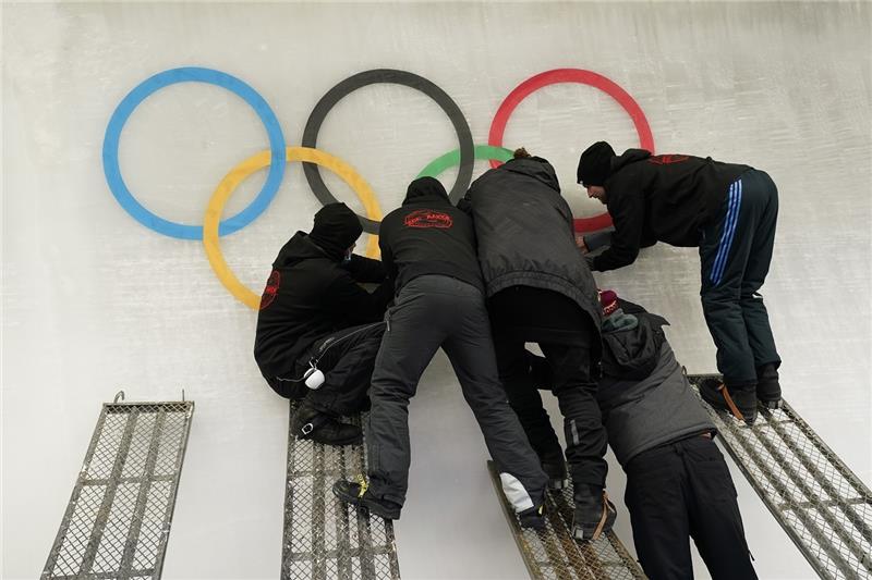 Arbeiter bringen im Vorfeld der Olympischen Winterspiele 2022 einen Ausschnitt der olympischen Ringe auf der Eisbahn des Yanqing National Sliding Center an. Foto: Jae C. Hong/AP/dpa