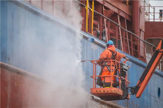 Arbeiter reinigen ein Frachtschiff auf dem Gelände der Werft.