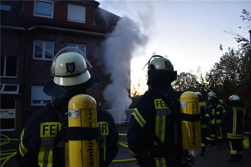 Atemschutzträger vor dem Löscheinsatz, im Hintergrund steigt der Rauch aus dem Keller eines Mehrfamilienhauses im Wohngebiet Kloster Dohren auf. Foto: Vasel