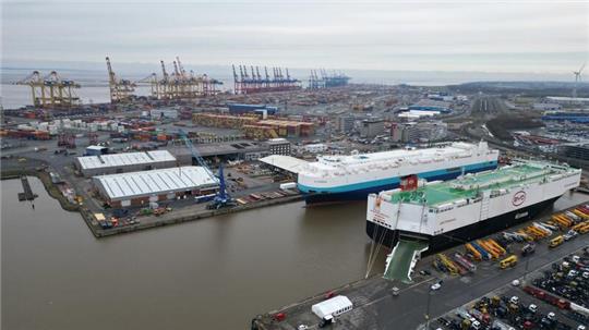 Auf dem Bild ist das Autoterminal in Bremerhaven zu sehen, im Hintergrund stehen Kräne des Containerterminals.
