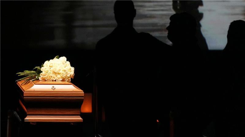 Auf dem Sarg liegt ein Strauß weißer Rosen.