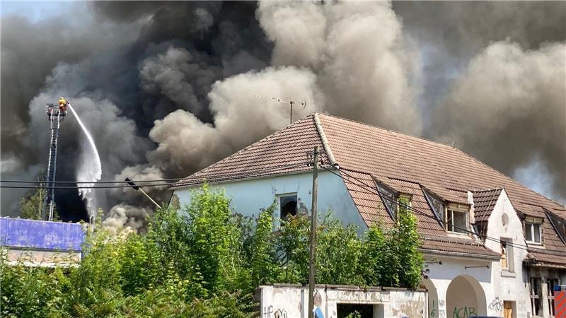 Auf dem alten Schlachthofgelände in Erfurt ist ein Feuer ausgebrochen und Rauch steigt in den Himmel, während die Feuerwehr gegen die Flammen kämpft.