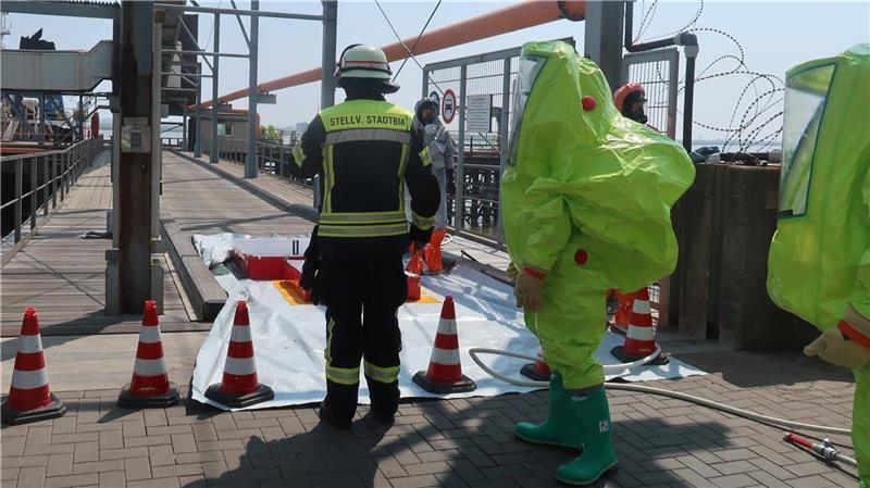 Auf der Glencore-Pier, auf der die Leckage entstanden ist, sind Helfer in spezieller Schutzkleidung im Einsatz. Foto: Polizei
