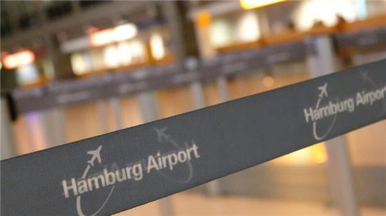 Auf einem Absperrband im Terminal 2 steht der Schriftzug „Hamburg Airport“, im Hintergrund befindet sich ein Serviceschalter der Lufthansa.