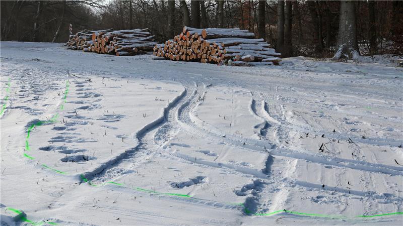 Auf einem schneebedeckten Feld sind Fahrzeugspuren im Schnee zu sehen.