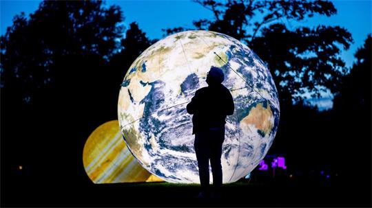 Auf einer Wiese im Park sind metergroße, beleuchtete Planeten zu sehen. 
