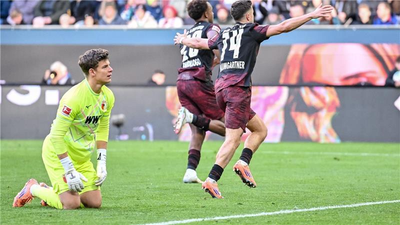 Augsburgs Torwart Finn Dahmen kauert bedröppelt am Boden, die Leipziger Assan Quedraogo (M) und Christoph Baumgartner (r) bejubeln das 0:5. 