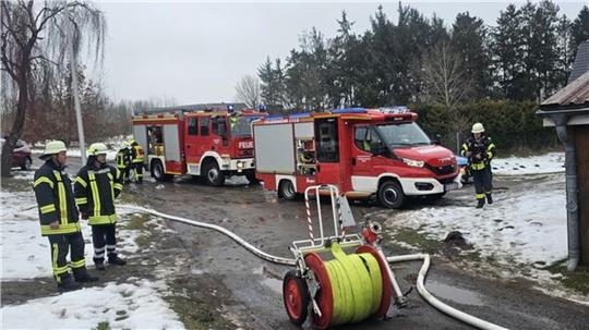 Aus wasserführenden Fahrzeugen werden Schlauchleitungen für einen Löschangriff aufgebaut, während sich Atemschutzgeräteträger ausrüsten.