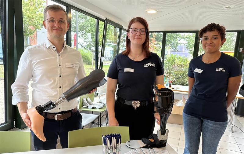 Ausbildungsleiter Jan-Hendrik Blasig präsentiert gemeinsam mit den Auszubildenden Jule Sommerfeld (Mitte) und Aurélie N'Kissi zwei Prothesen am Stand von Incort.