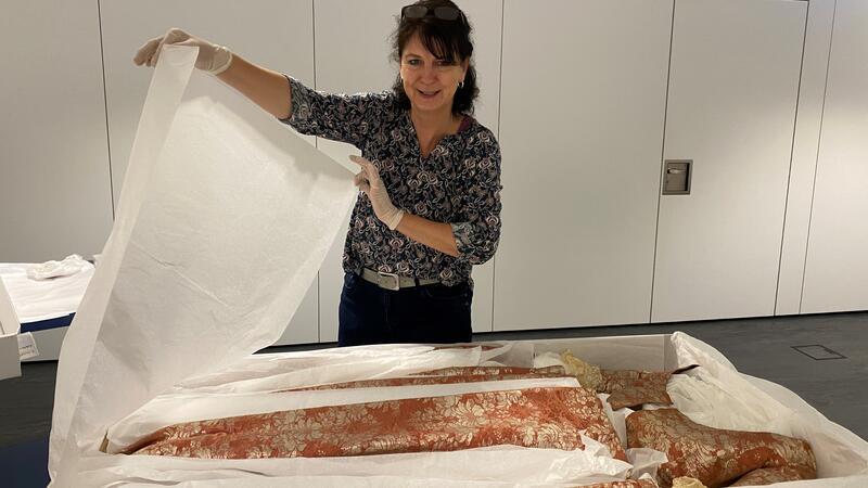 Mit Handschuhen hebt Das kostbare Seidenkleid aus dem 18. Jahrhundert