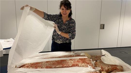 Mit Handschuhen hebt Das kostbare Seidenkleid aus dem 18. Jahrhundert