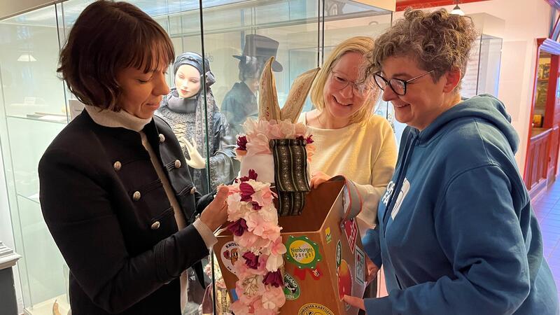 Ausstellungsvorbereitung: Miriam Stöckmann, Dr. Kai Janofsky und Barbara Wetegrove (von links) schauen in die Kiste mit dem Flunkkranz, neben der Filigrankette das Symbol der Würde der Blütenkönigin.