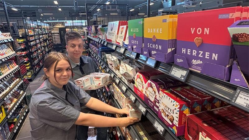 Auszubildende Miley Beier und Rewe-Mitarbeiter Niklas Niemand räumen in der Süßwarenabteilung Schokoladenartikel in das Regal.
