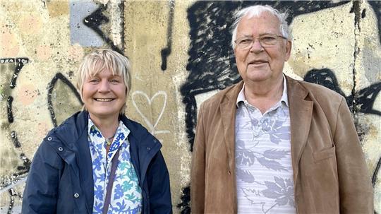 Maja Nielsen und Joachim Neumann stehen vor einem noch erhaltenen und mit Grafitti besprühten Teil der Berliner Mauer.