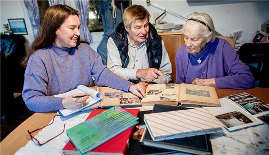 Autorin Susanne Hinrichs (l) betrachtet gemeinsam mit Wolf-Rüdiger und Ilse Baerwinkel die alten Fotos in den Fotoalben des Ehepaars. Die Autorin Susanne Hinrichs verfasst Biografien im Auftrag von Menschen, die nicht berühmt sind, aber dennoch eine professionell verfasste Lebensgeschichte für ihre Nachfahren hinterlassen möchten. Foto: Hauke-Christian Dittrich/dpa