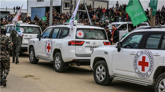 Autos des Internationalen Roten Kreuzes stehen im Februar 2025 bereit, während Kämpfer der Al-Kassam-Brigaden, des militärischen Flügels der islamistischen Terrororganisation Hamas, israelische Geiseln an Vertreter des Internationalen Komitees vom Roten Kreuz (IKRK) übergeben.